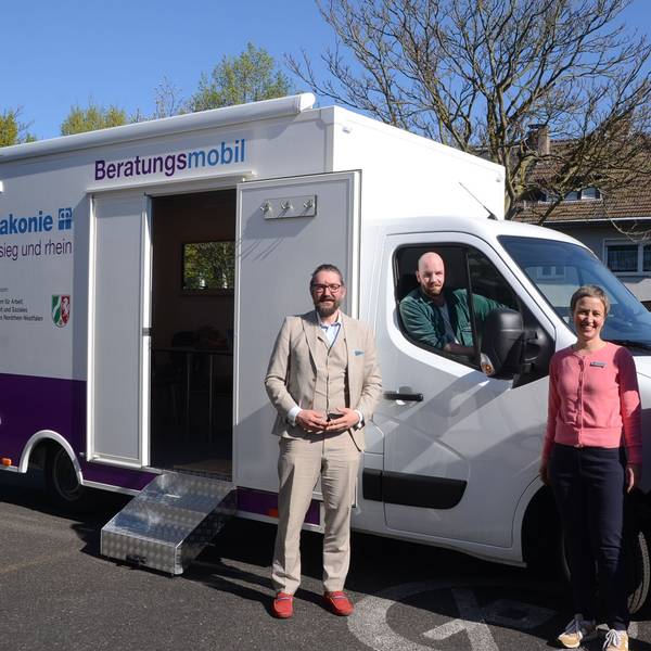 Zwei Frauen und ein Mann stehen vor einem Kleinlaster mit einem Containeraufbau, ein zweiter Mann sitzt im Führerhaus. Auf dem Aufbau steht Diakonie Beratungsmobil.