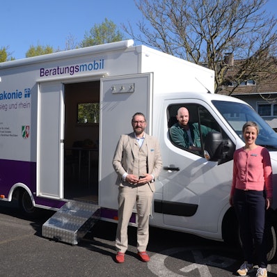 Zwei Frauen und ein Mann stehen vor einem Kleinlaster mit einem Containeraufbau, ein zweiter Mann sitzt im Führerhaus. Auf dem Aufbau steht Diakonie Beratungsmobil.