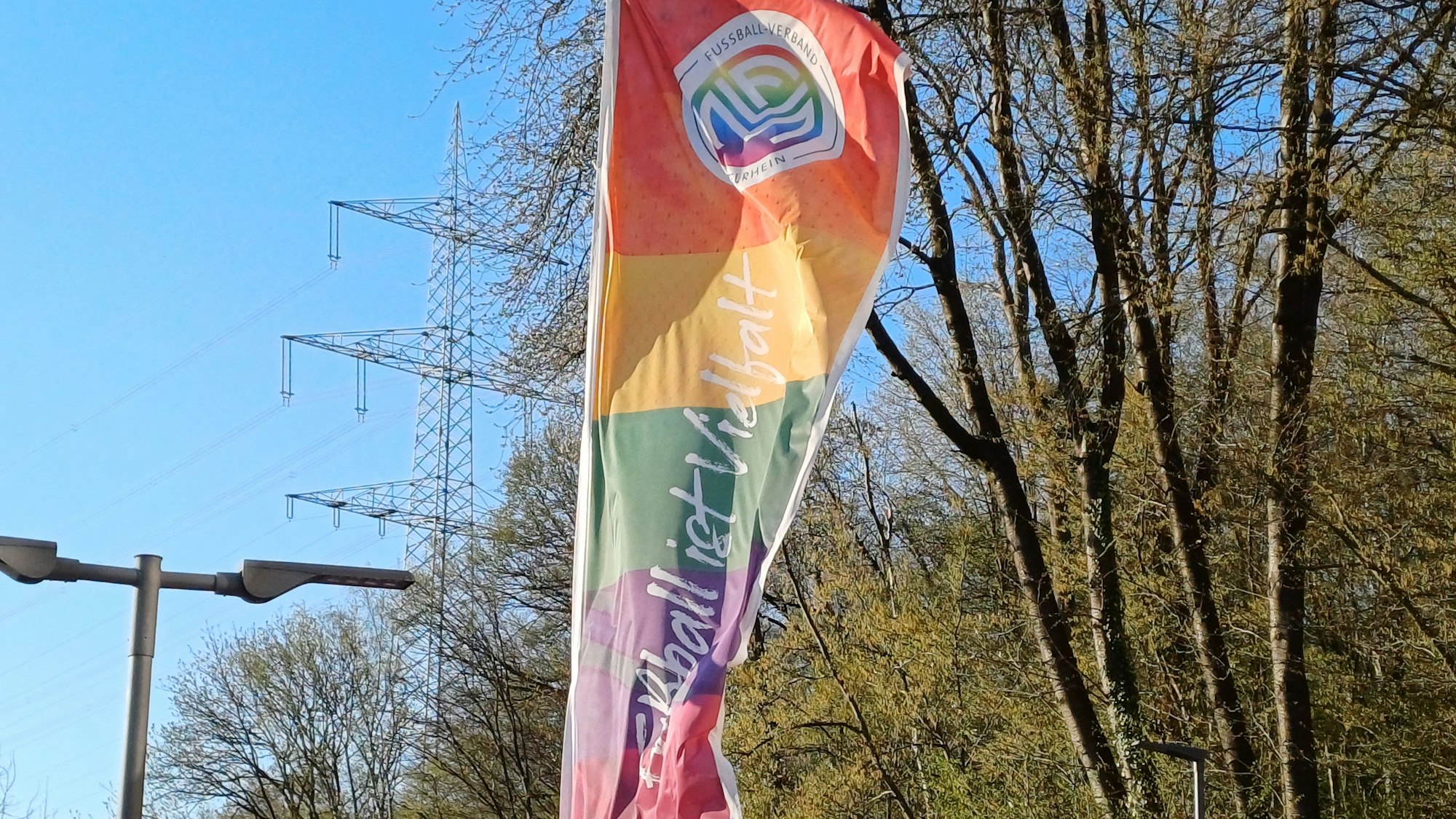 Auf einer Flagge des Fußball-Verbands Mittelrhein im Regenbogenmuster steht „Fußball ist Vielfalt“.
