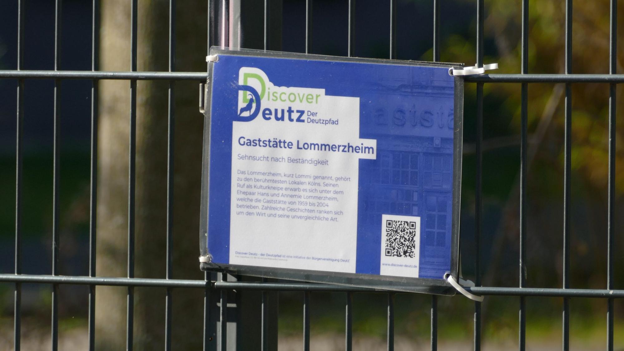 Eine Tafel mit einem QR-Code hängt an einem Zaun.