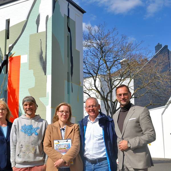 Zwei Frauen und vier Männer stehen in einer Reihe vor dem Parkhaus mit dem künstlerisch gestalteten Treppenhausturm.