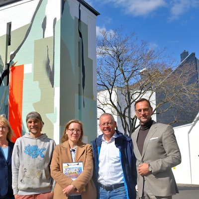 Zwei Frauen und vier Männer stehen in einer Reihe vor dem Parkhaus mit dem künstlerisch gestalteten Treppenhausturm.