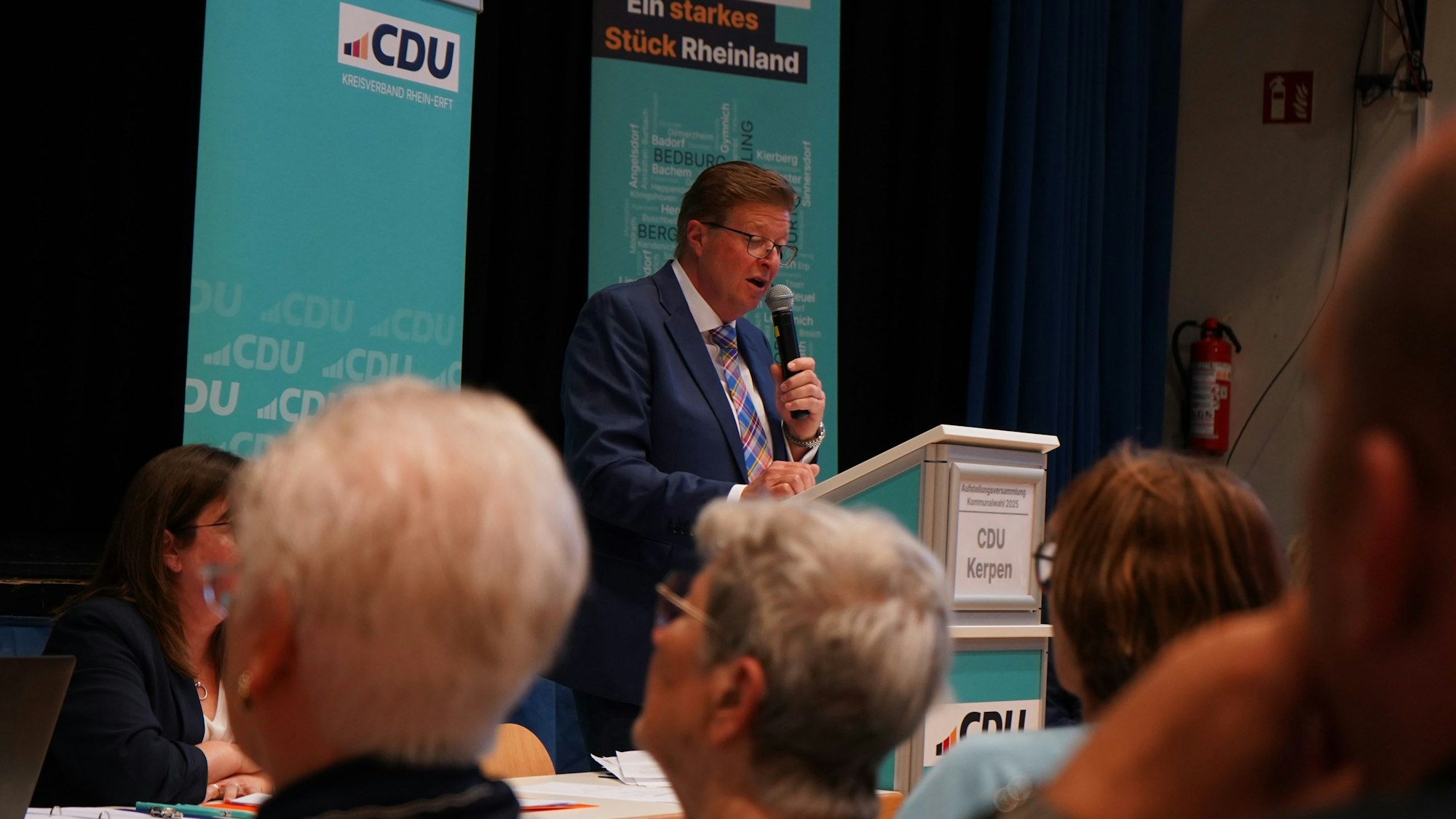 Ein Mann redet mit einem Mikrofon zu einem Publikum.