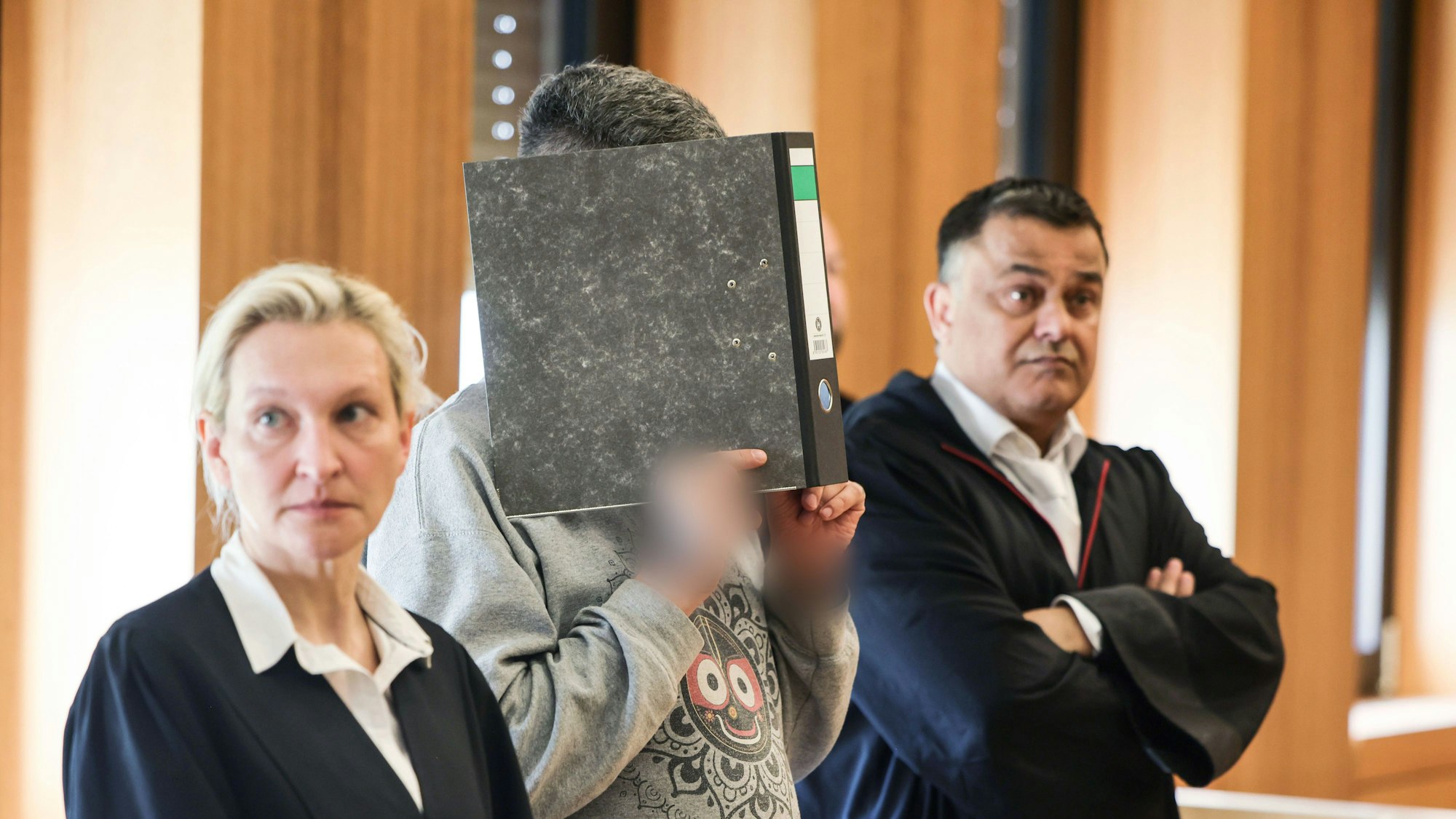 Der angeklagte Krankenpfleger hält sich zwischen seinen Anwälten Volker Breyer (r) und Tanja Tomasso (l) einen Aktenordner vor das Gesicht. Ulrich S. steht wegen Mordes an neun Patienten vor dem Aachener Landgericht.