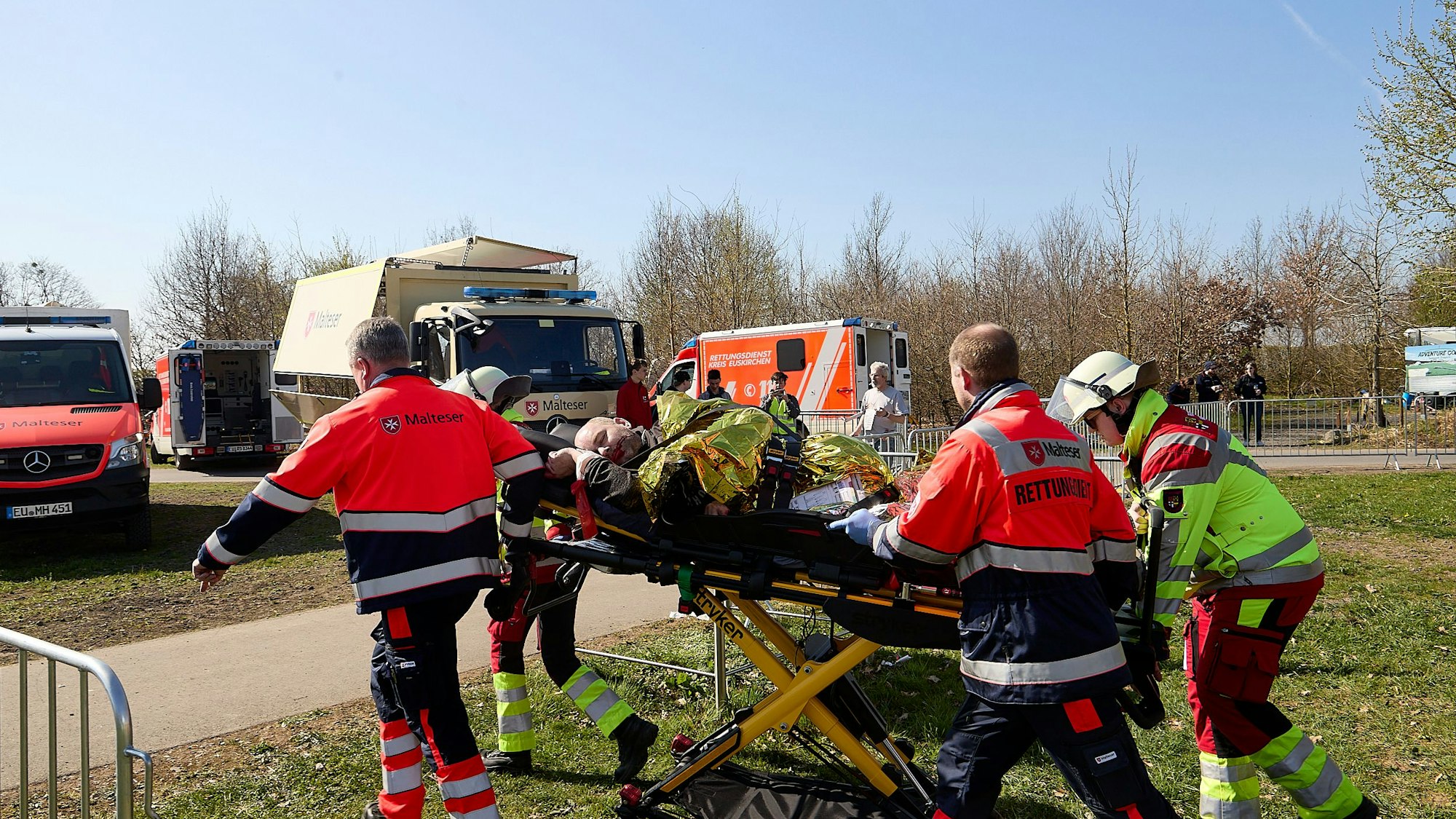 Vier Rettungskräfte transportieren einen Mann auf einer Krankentrage zu einem Rettungswagen.