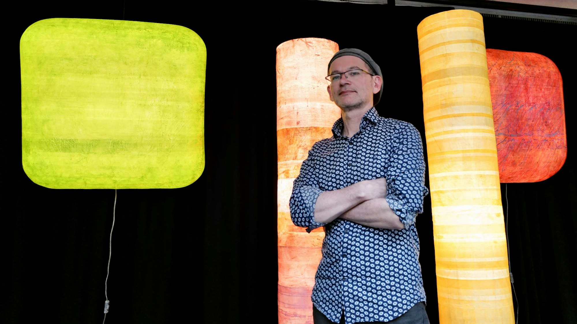 Ein Mann steht zwischen farbigen Leuchtobjekten auf einer Bühne.