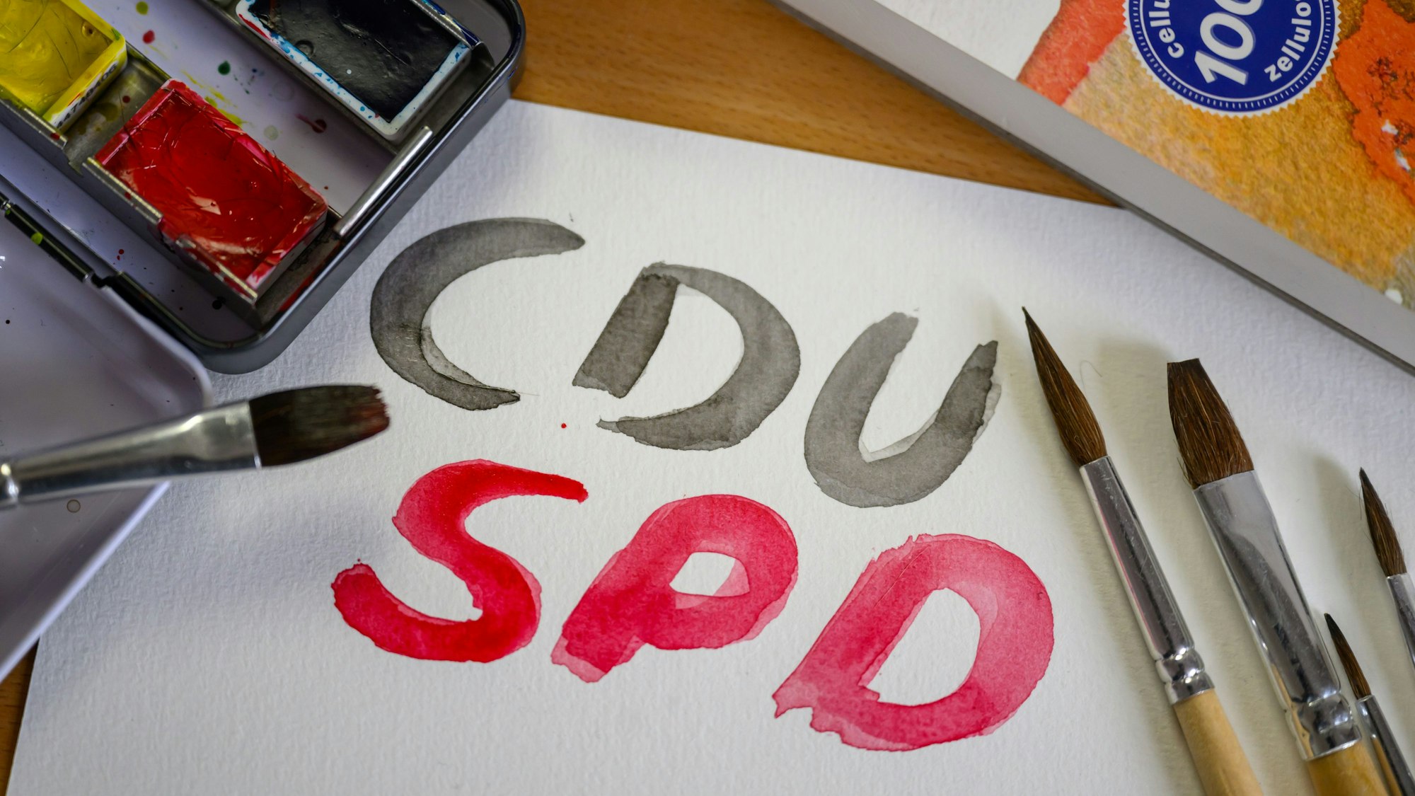 Mit Wasserfarben stehen die Namen der Parteien CDU und SPD auf einem Blatt Aquarellpapier.