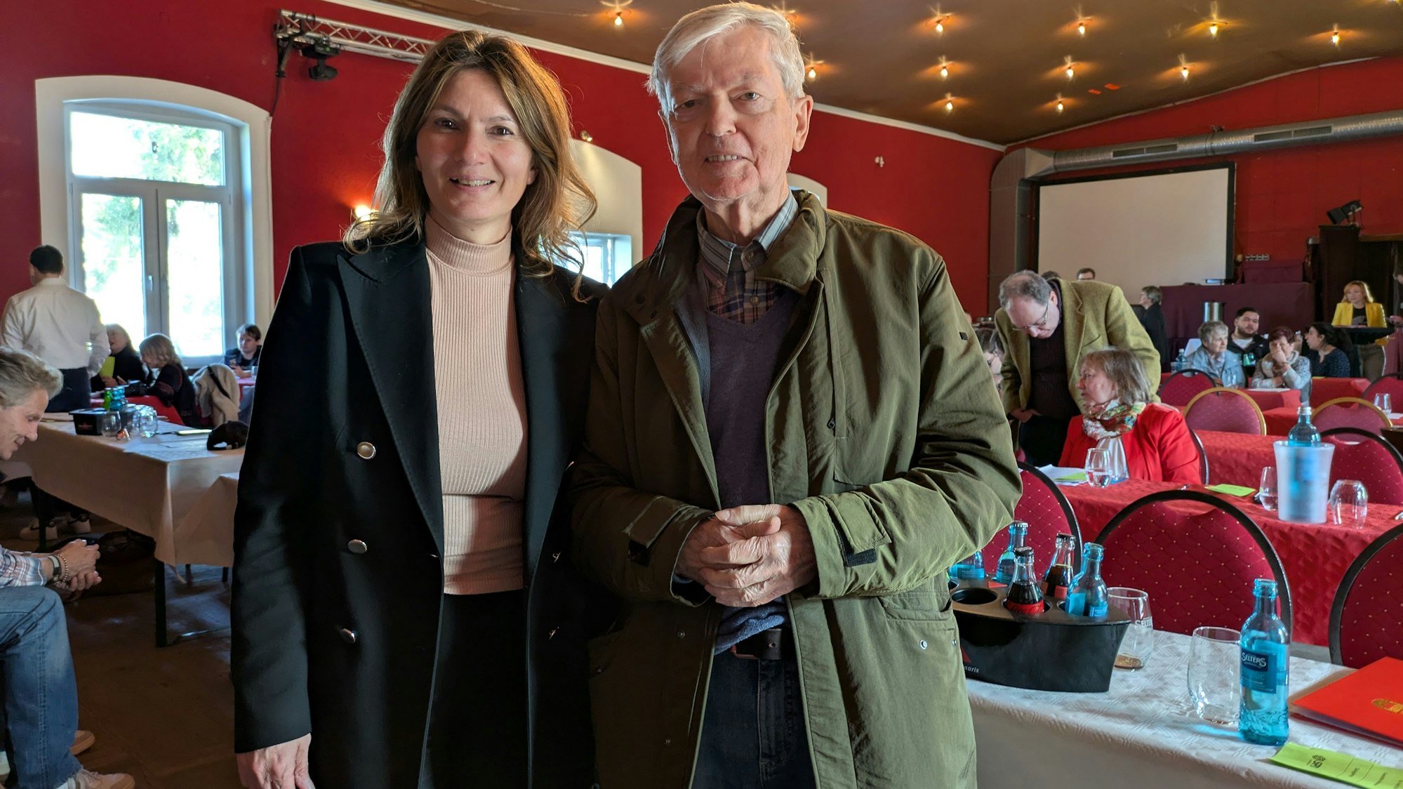 Ein Mann und eine Frau stehen in einem Saal mit Tischreihen.