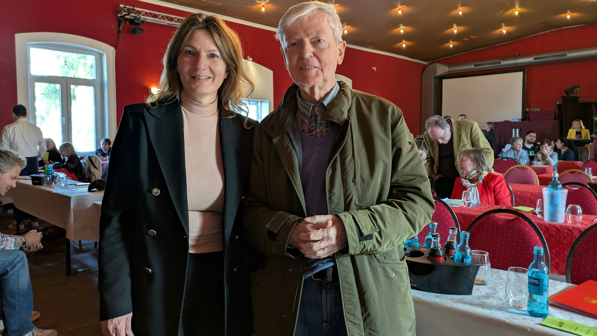 Ein Mann und eine Frau stehen in einem Saal mit Tischreihen.