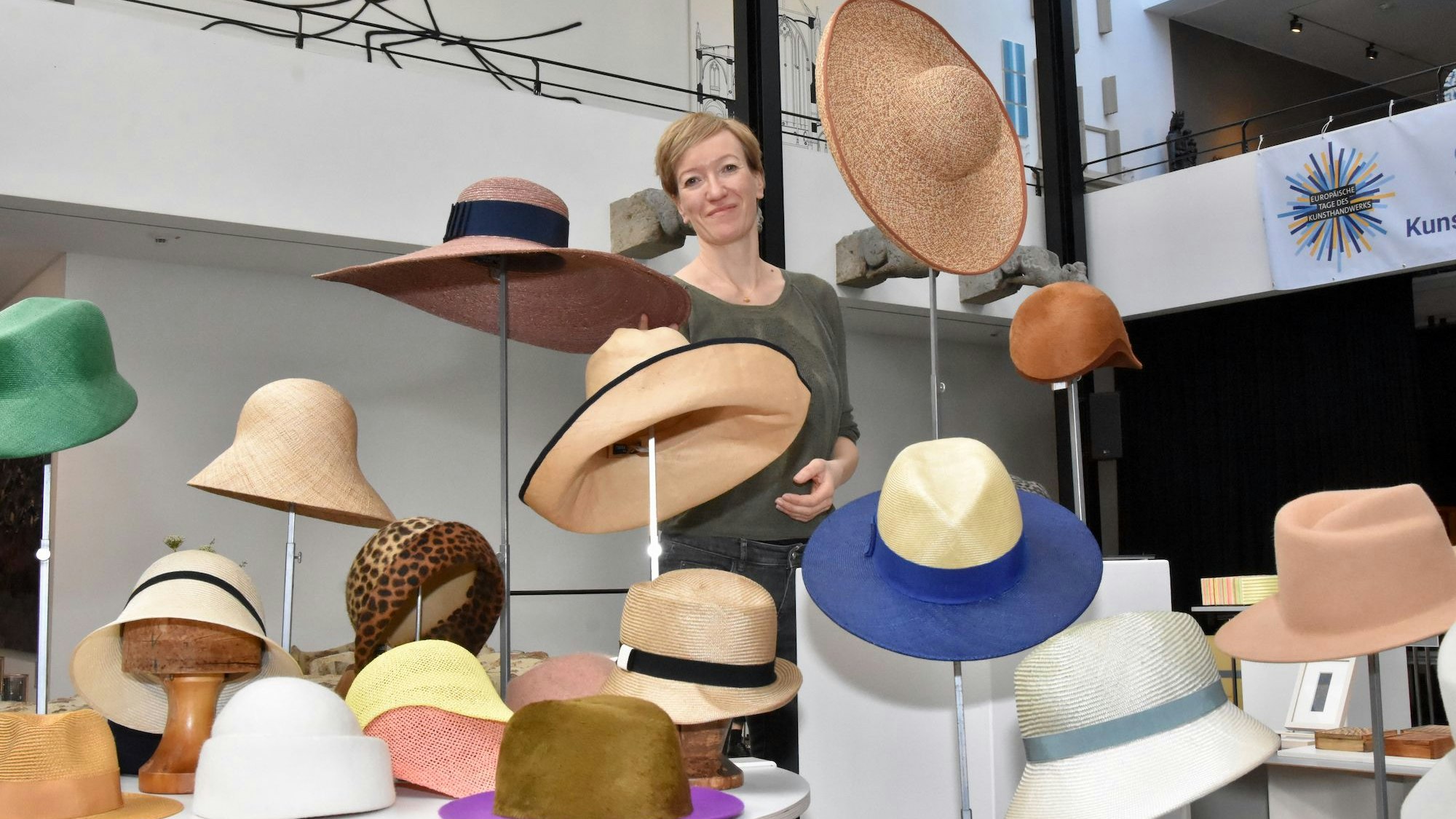 Eine Frau steht hinter einer Präsentation von unterschiedlichen Hüten.
