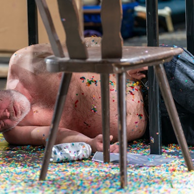 Jan Höppner liegt als Götz von Berlichingen mit freiem Oberkörper, scheinbar betrunken schlafend, unter einem Tisch.