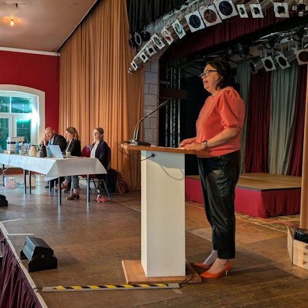 Eine Frau steht an einem Rednerpult auf einer Bühne.