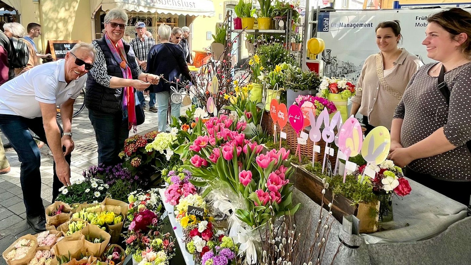 Zu sehen sind Sarah Berke und Maria Gabriel an einem Verkaufsstand mit bunten Blumen.