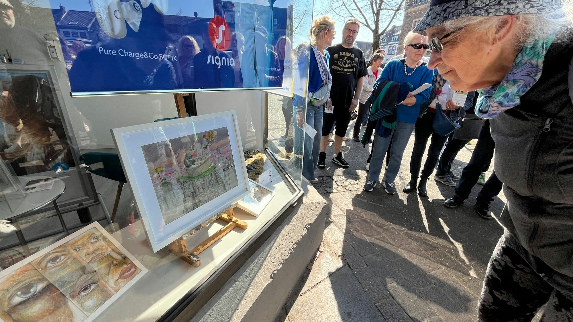 Auf dem Bild sind Passanten zu sehen, die sich Kunstwerke in einem Schaufenster ansehen.