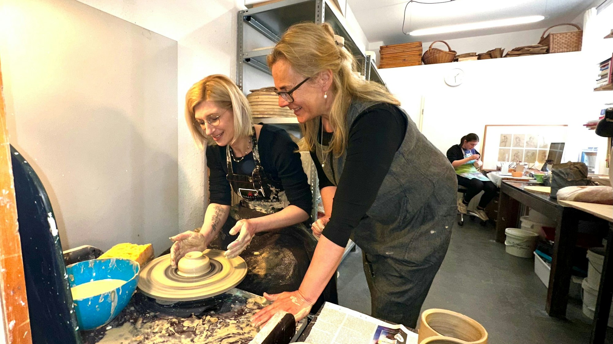 Zwei Frauen an der Töpferscheibe in einer Werkstatt.