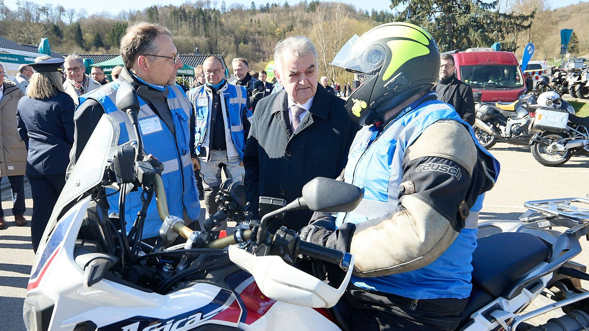 NRW-Innenminister Herbert Reul ist im Gespräch mit einer Person, die einen Helm trägt und auf einem Motorrad sitzt, sowie einem weiteren Mann, der eine blaue Warnweste trägt.