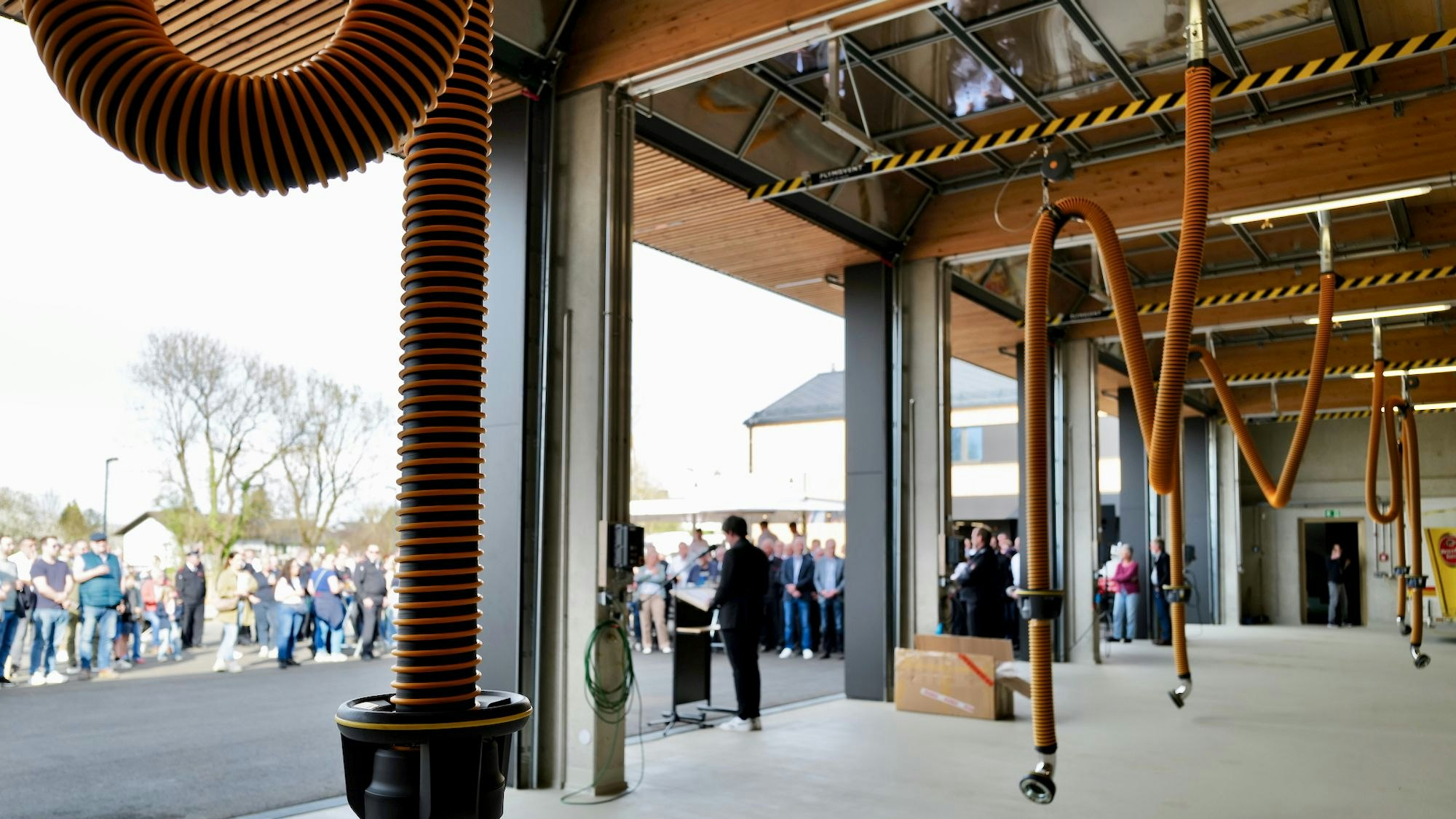 Blick ins Freie aus einer Fahrzeughalle heraus. Von der Decke hängen dicke Schläuche.