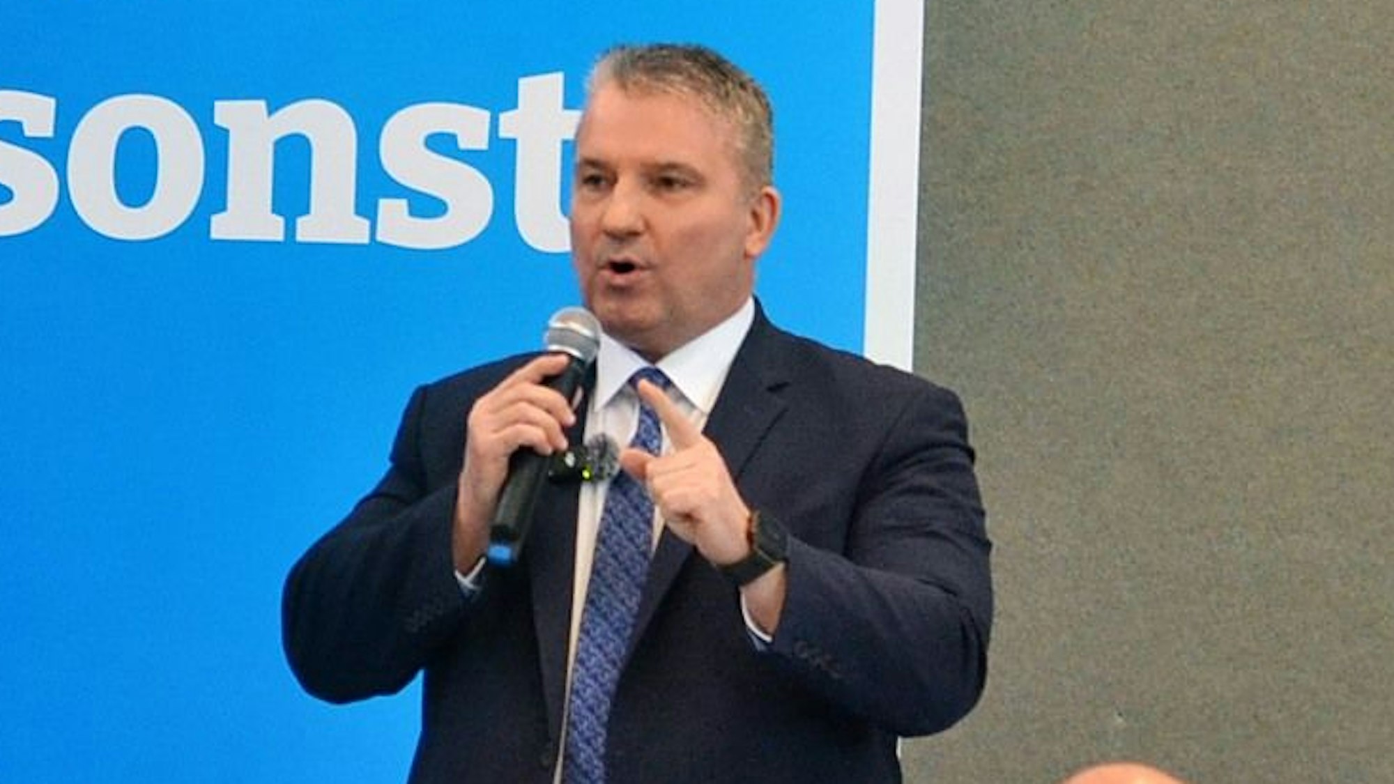 Das Bild zeigt Martin Hess, der durch ein Mikrofon zum Publikum spricht.