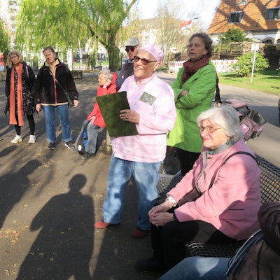 Menschen stehen im Halbkreis auf einem großen Vorplatz, eine Frau mit rosa Mütze referiert.