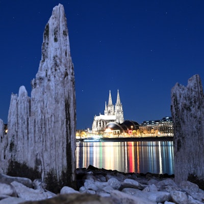 Teile einer Holzkonstruktion, die normalerweise unter Wasser liegen, sind in der Nacht zum Montag (7. April) am Rhein zu sehen. Der Kölner Dom im Hintergrund.