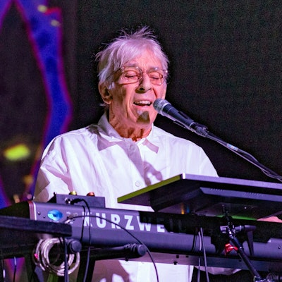John Cale spielt Keyboard und singt auf der Bühne des Carlswerk Victoria. Er trägt ein weißes Hemd und Brille.