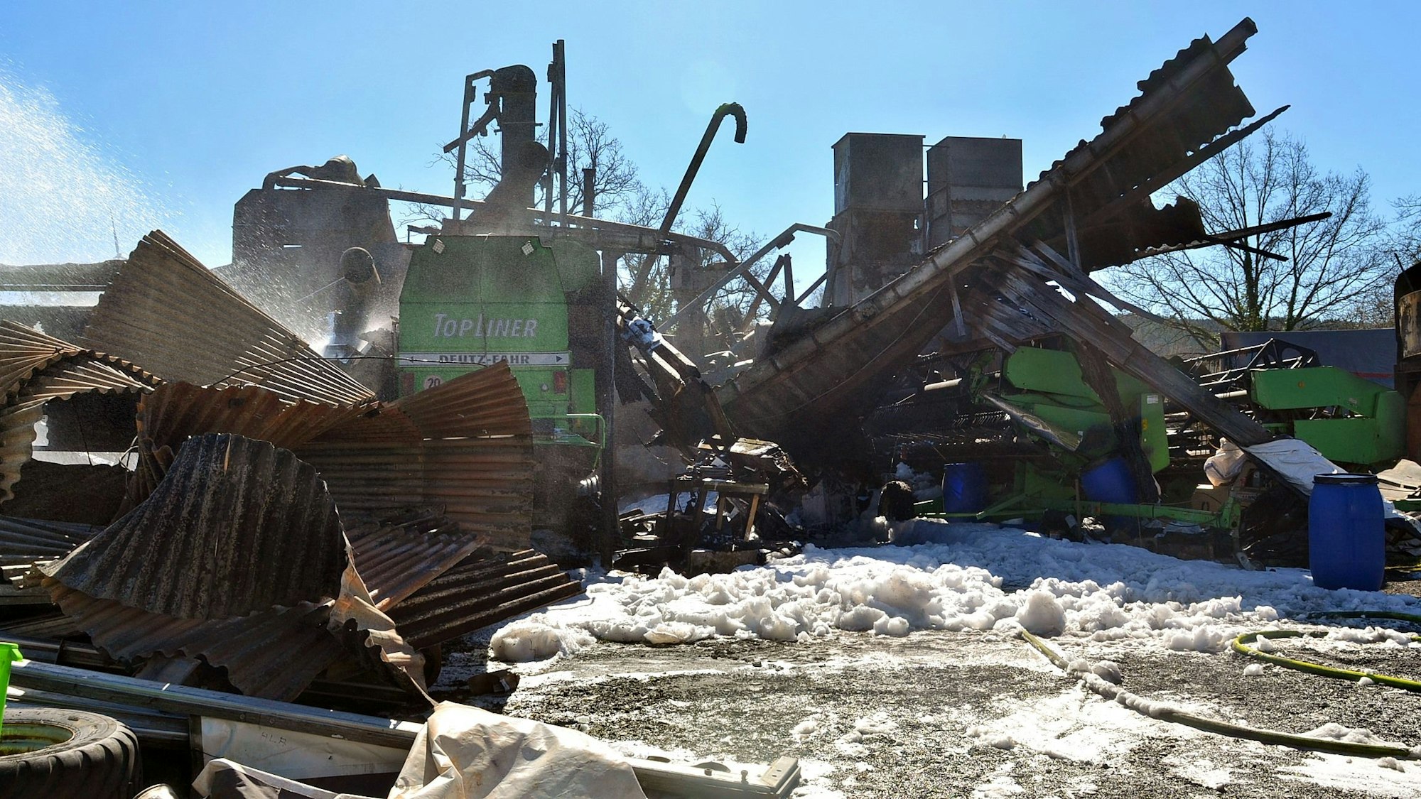 Das Heck eines grünen Mähdreschers ist in den Trümmern der Halle zu sehen, die in Kall-Scheven niedergebrannt ist.