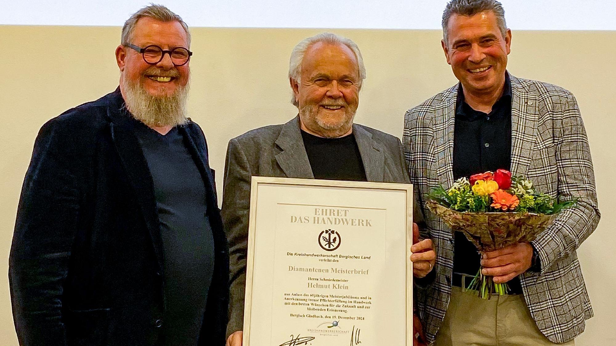 Zwei Männer überreichen einen Diamantenen Meisterbrief an Helmut Klein.