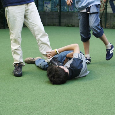 Zwei Jugendliche treten auf einen am Boden liegenden Jungen ein.