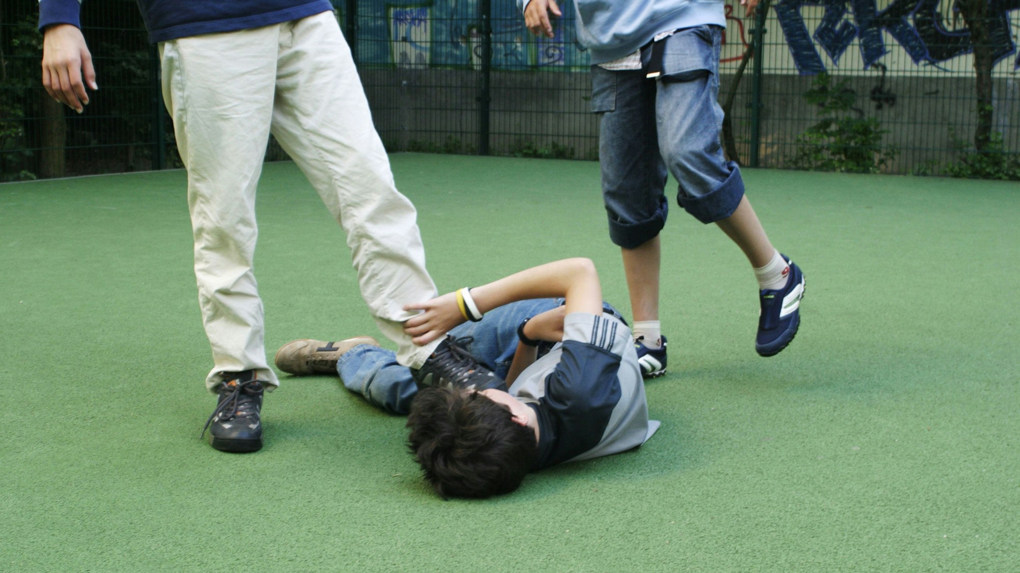 Zwei Jugendliche treten auf einen am Boden liegenden Jungen ein.