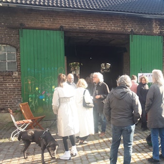 Eine Gruppe Menschen steht vor einem Hofgebäude mit großen grünen Holztüren.
