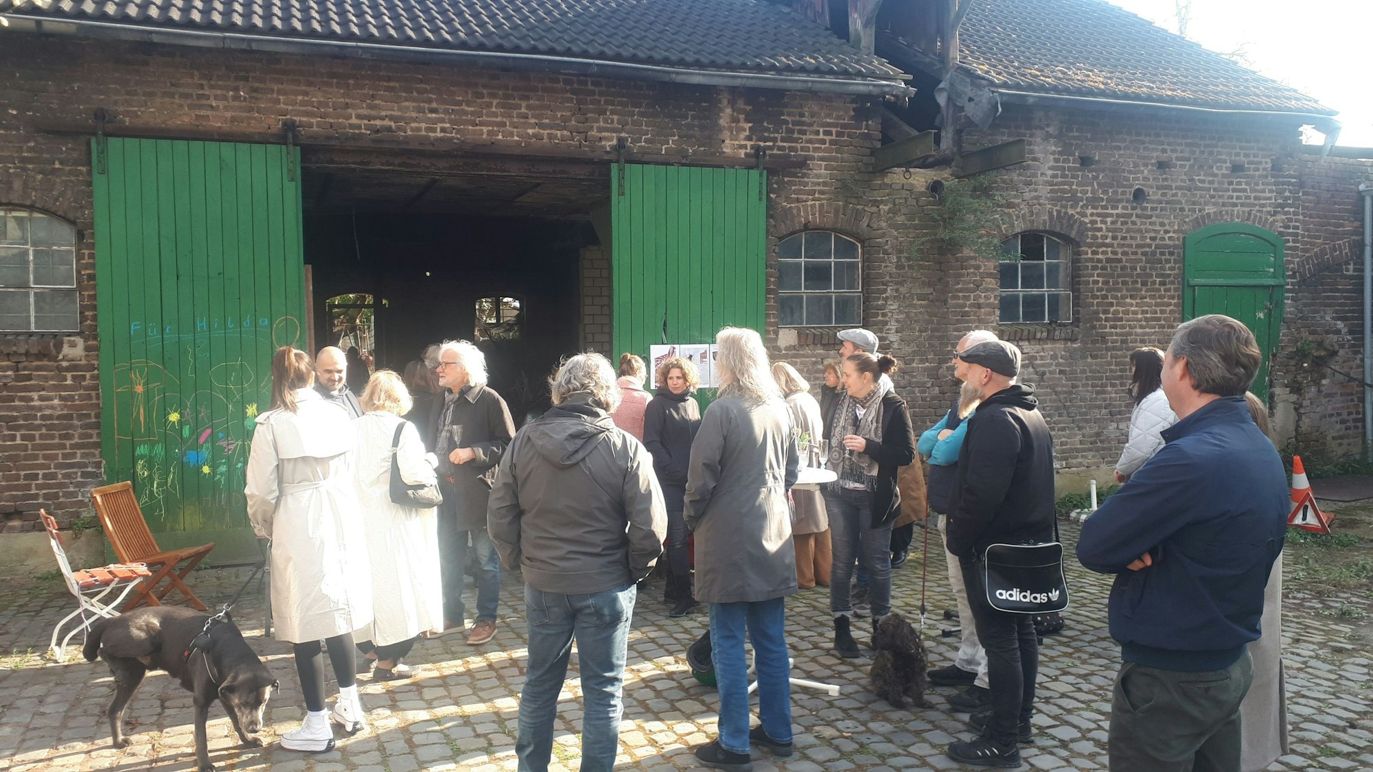 Eine Gruppe Menschen steht vor einem Hofgebäude mit großen grünen Holztüren.