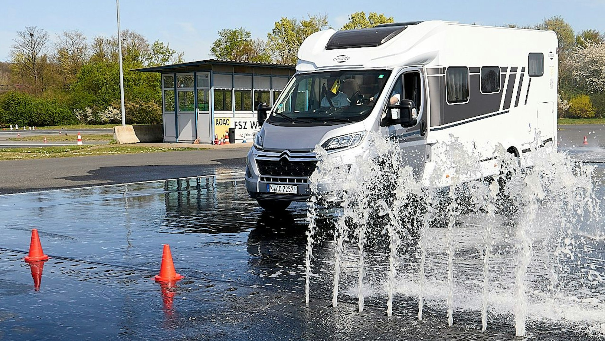 Ein Campingwagen fährt durch eine große Pfütze. Wasser spritzt aus dem Boden.