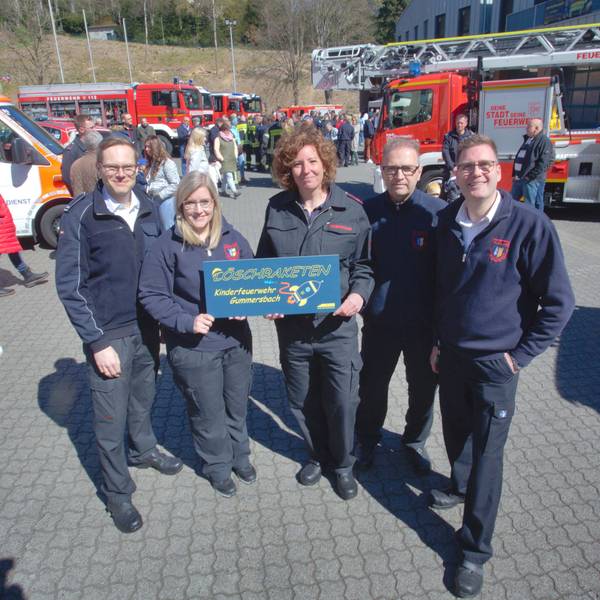 Mehrere Mitglieder der Feuerwehr halten gemeinsam ein Schild hoch, auf dem der Name der neuen Gummersbacher Kinderfeuerwehr, „Löschraketen“, steht.