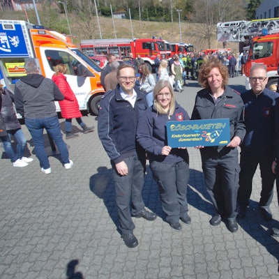 Mehrere Mitglieder der Feuerwehr halten gemeinsam ein Schild hoch, auf dem der Name der neuen Gummersbacher Kinderfeuerwehr, „Löschraketen“, steht.