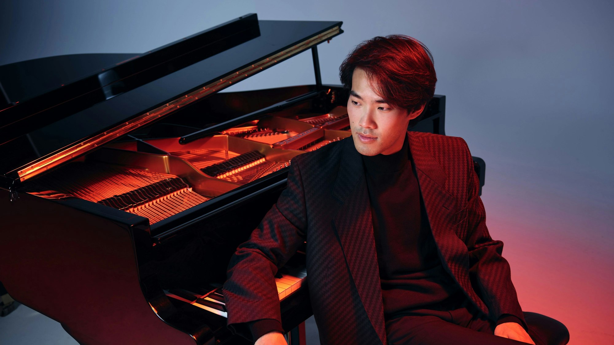 Gegen sein Klavier gelehnt sitzt der Pianist Bruce Liu.