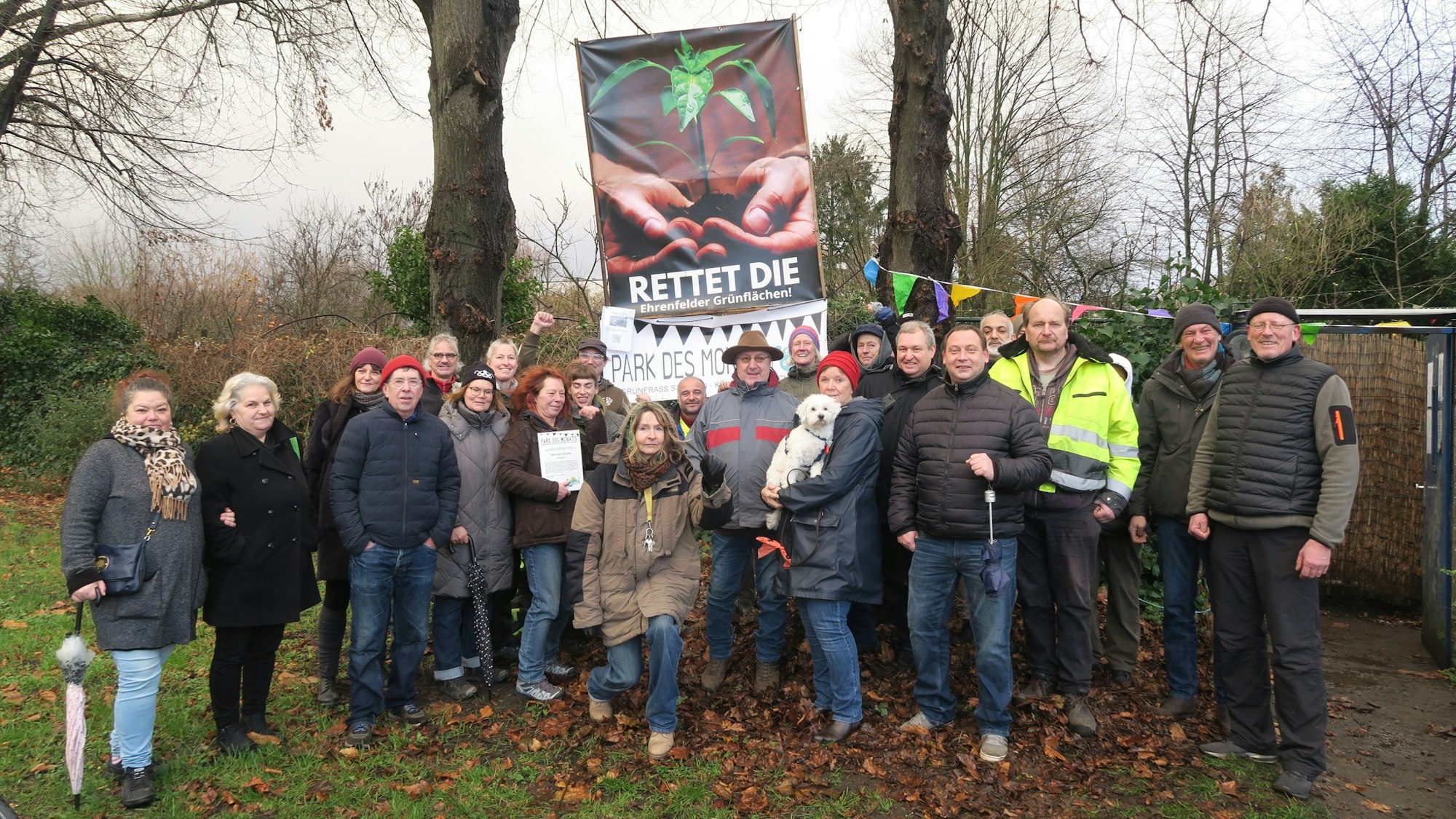 Viele Personen stehen auf einer Wiese einer Kleingärten-Anlage.