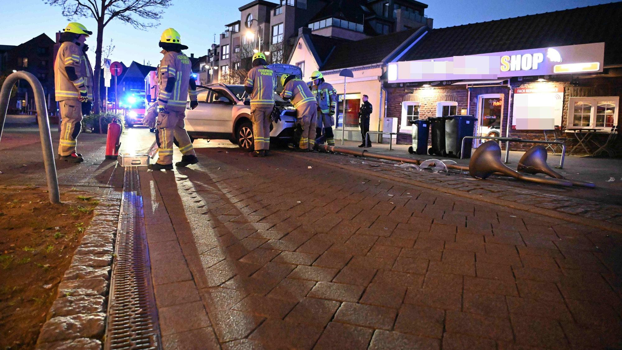 Feuerwehrleute stehen in der Nähe eines Pkw, der mit einer Straßenlaterne kollidiert war.