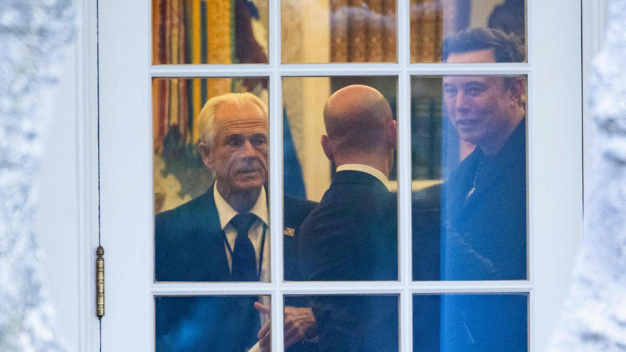 Das Bild zeigt Peter Navarro, Stephen Miller und Elon Musk bei Gesprächen an einem Fenster im Weißen Haus.