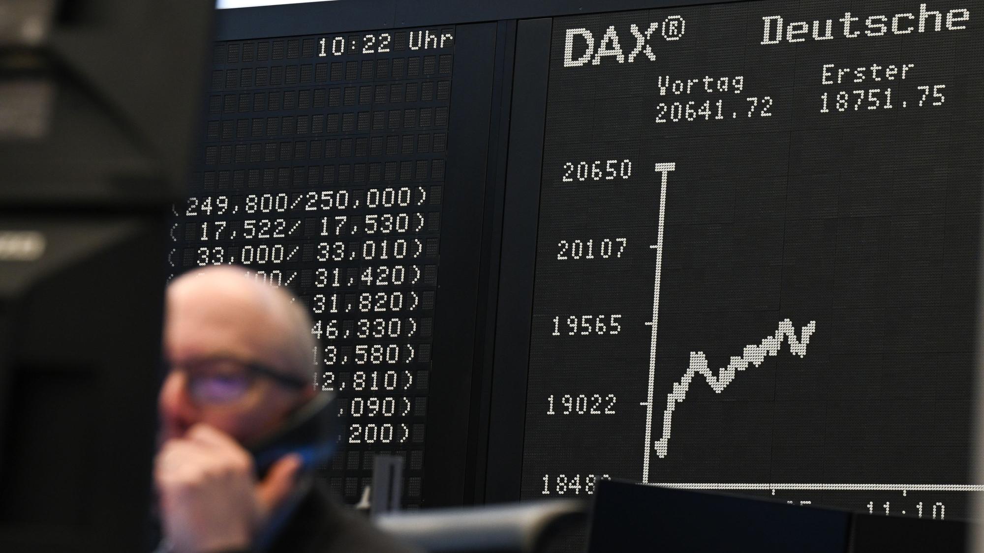 Während ein Börsenhändler auf dem Parkett der Frankfurter Börse vor seinen Monitoren sitzt, zeigt die Anzeigetafel mit der Dax-Kurve einen Wert von unter 20.000 Punkten an.