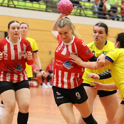 Corinna Schmitz beim Wurf. Eine Gegenspielerin hinter ihr versucht sie noch zu packen, eine Gegenspielerin, die von der Seite kommt, ebenfalls.