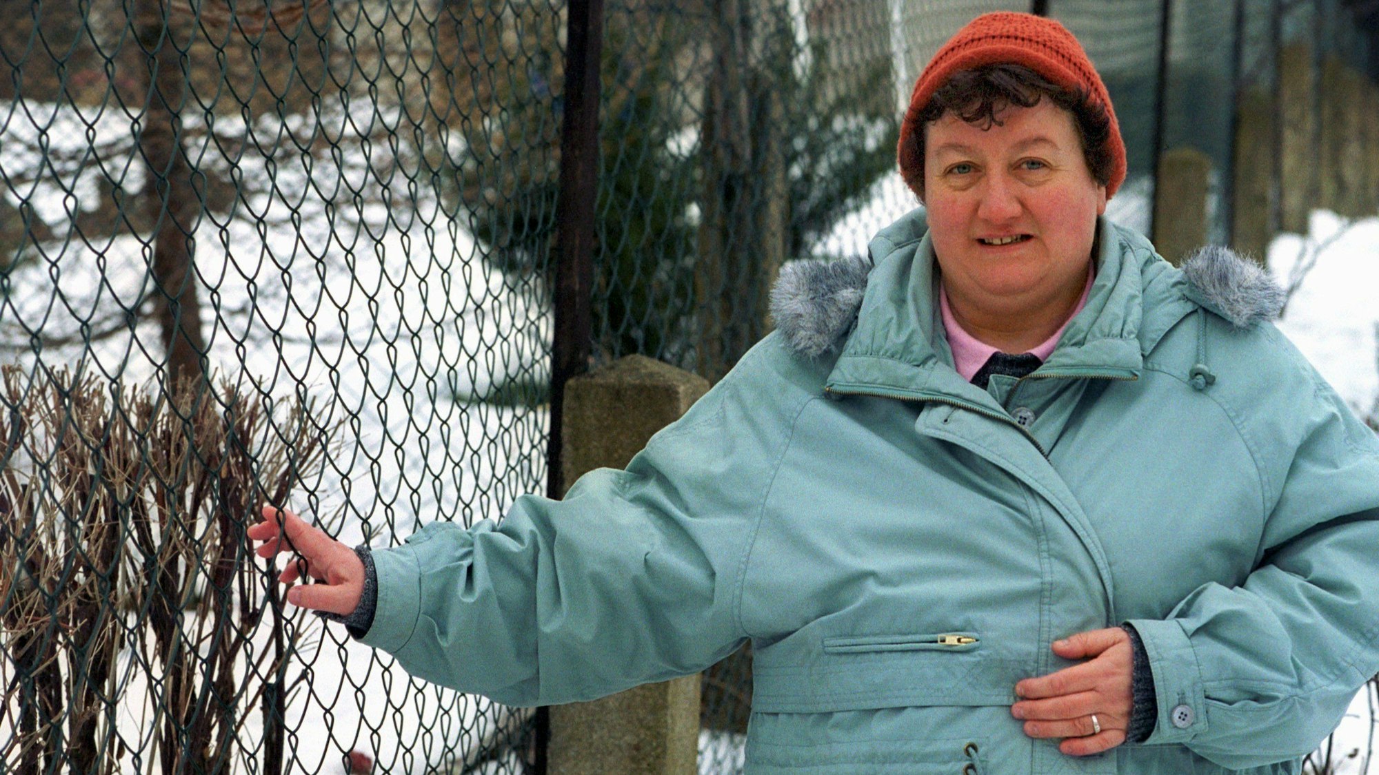 An ihrem Maschendrahtzaun steht Hausfrau Regina Zindler in hellblauer Jacke und roter Mütze.