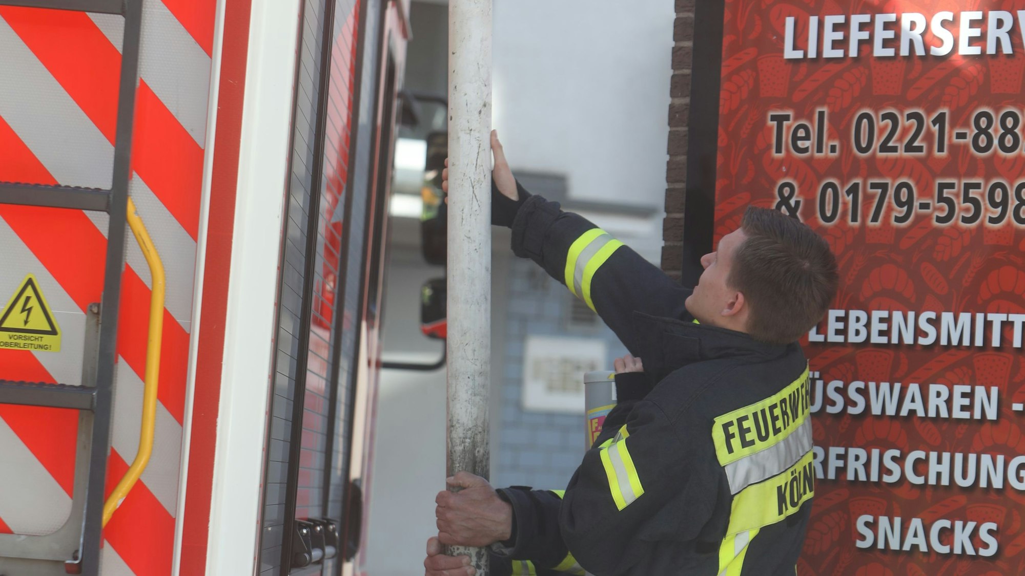 Zu sehen ist ein Feuerwehrmann, der neben einem Feuerwehrauto steht und an einem Pfosten zieht.