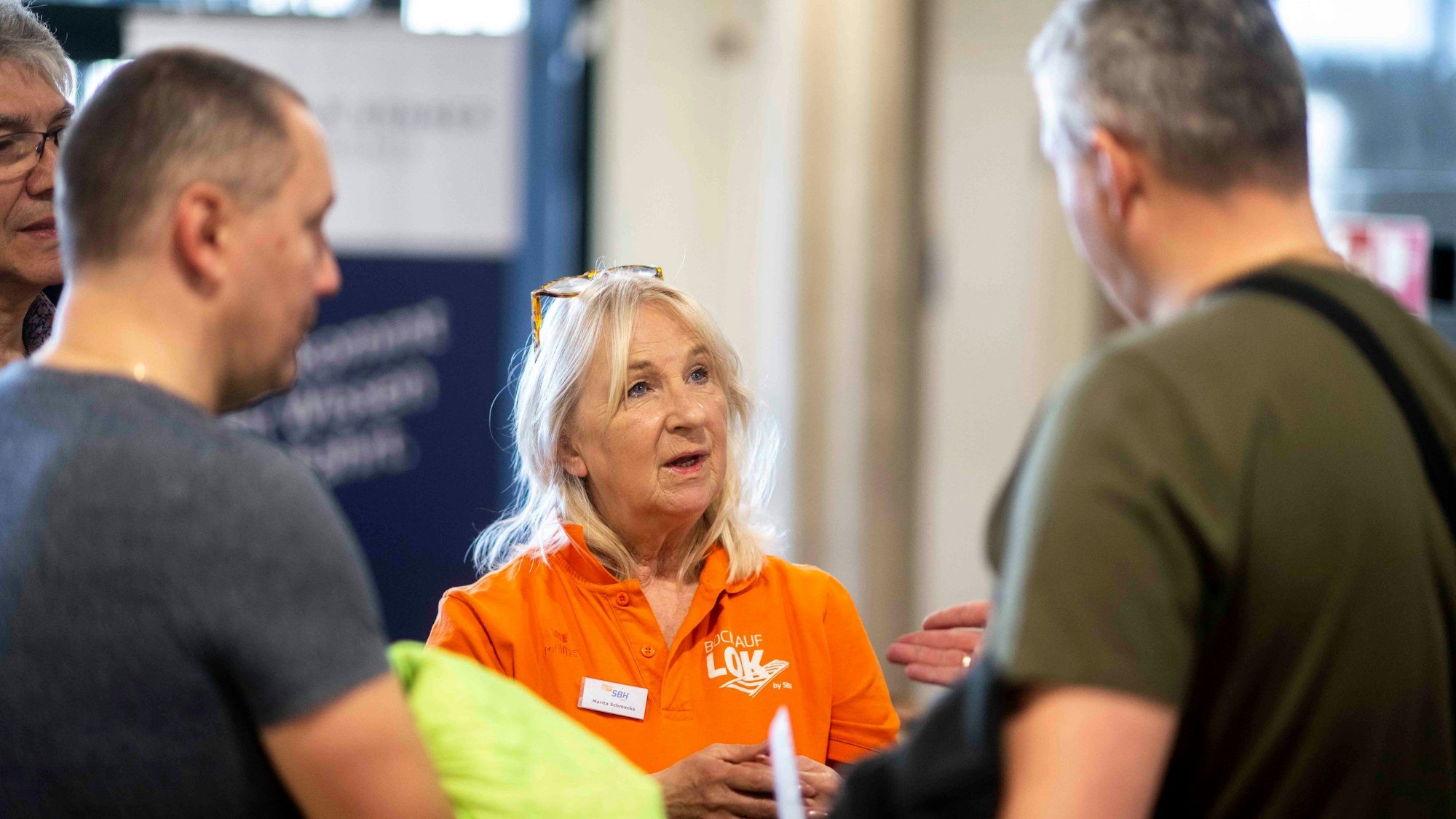 Das Bild zeigt Marita Schmacks im Gespräch mit zwei Männern.