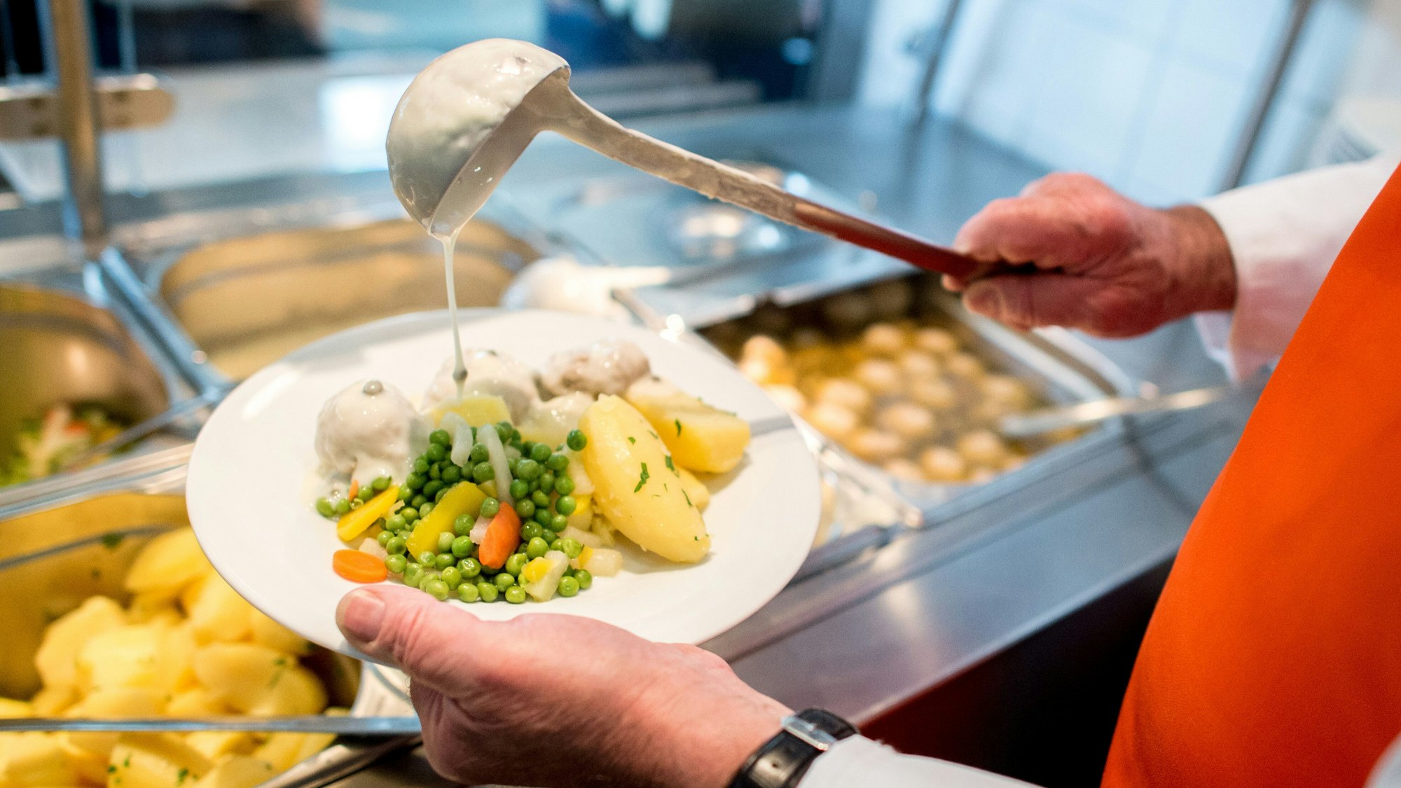 Ein Mitarbeiter bereitet in einem Betriebsrestaurant ein Tellergericht mit Königsberger Klopsen zu.