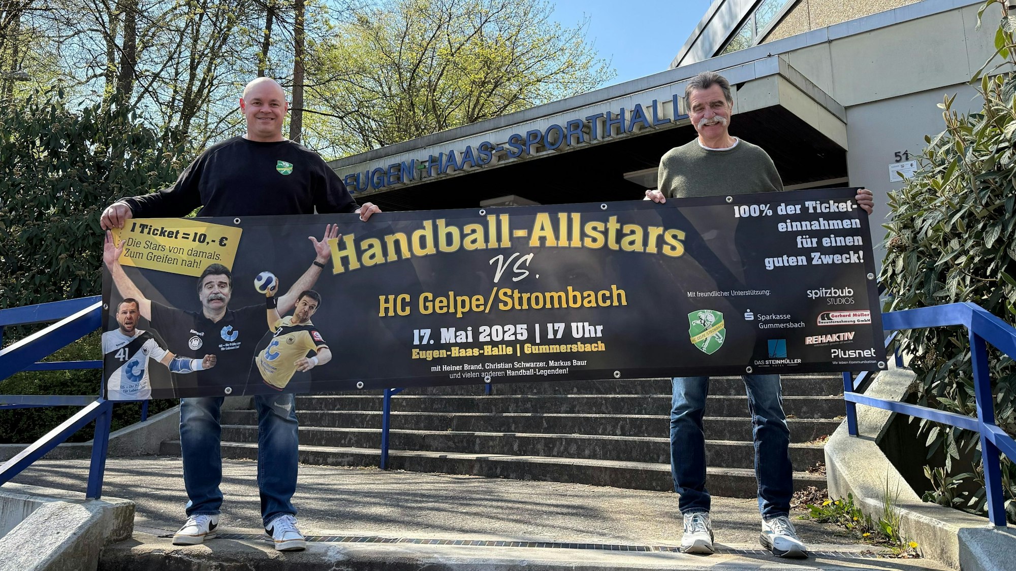 Dass Bild zeigt zwei Handballer, die ein Werbebanner hochhalten.
