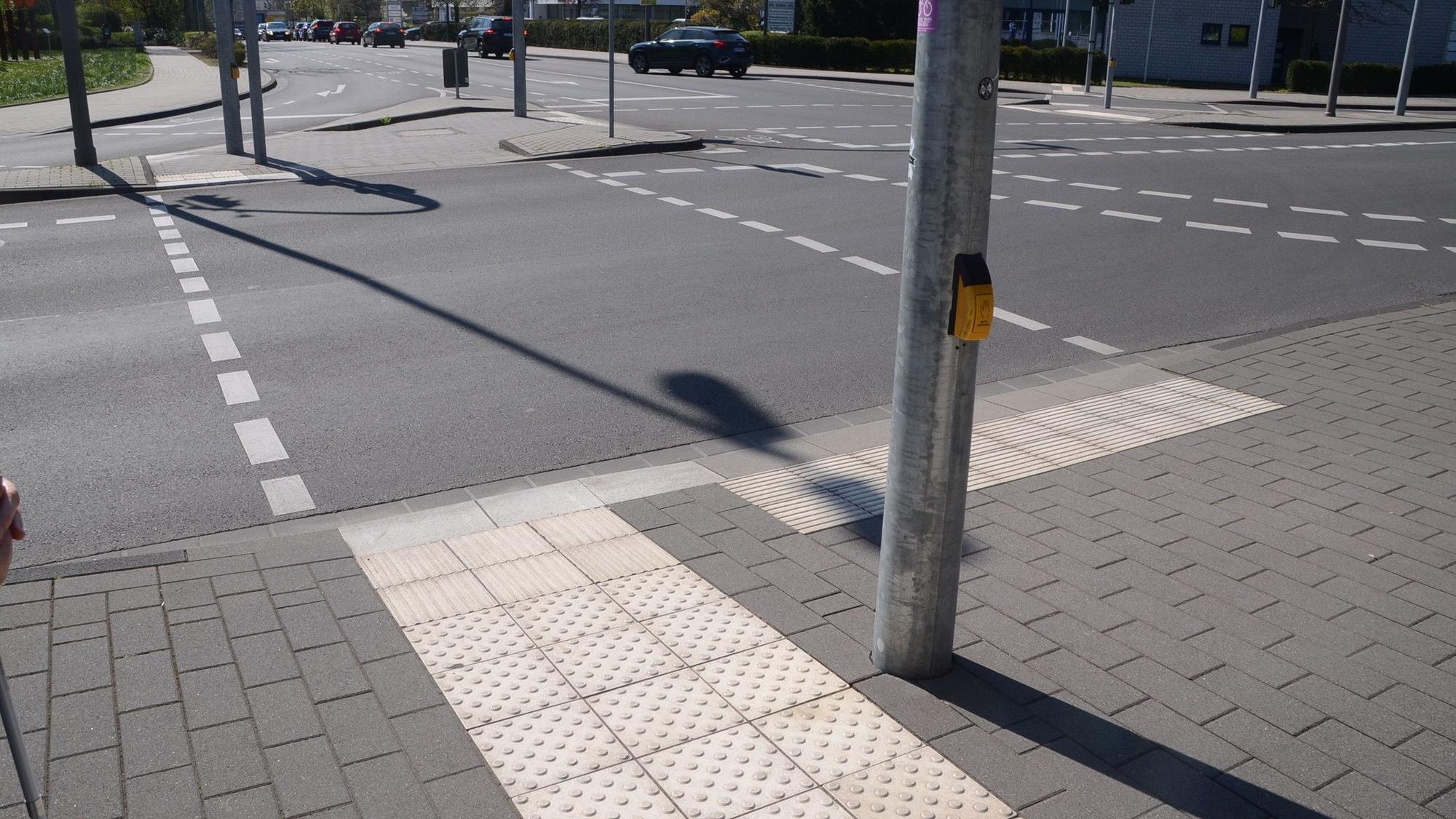 Ein Überweg an der Stadthalle: links der Streifen für Sehbehinderte und Blinde, die abschließende Kante ist drei Zentimeter hoch und mit dem Stock tastbar. Rechts gibt es keine derartige Kante und mit den Querrillen das Signal, stehen zu bleiben.