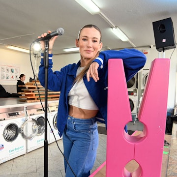 Zu sehen ist Jeannine Michaelsen im Zollstocker Waschsalon. Sie schaut mit Mikrofon in die Kamera.