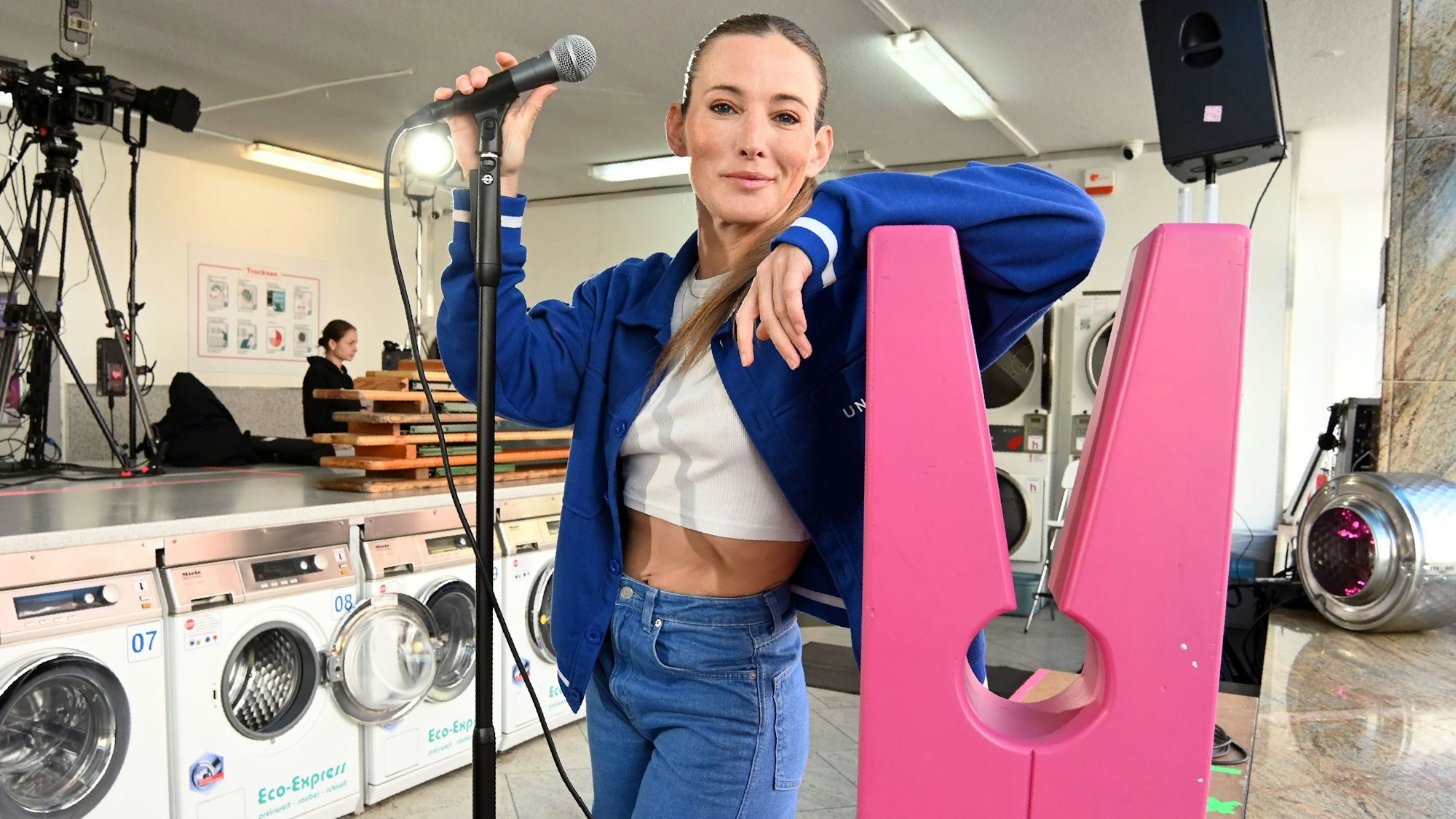 Zu sehen ist Jeannine Michaelsen im Zollstocker Waschsalon. Sie schaut mit Mikrofon in die Kamera.