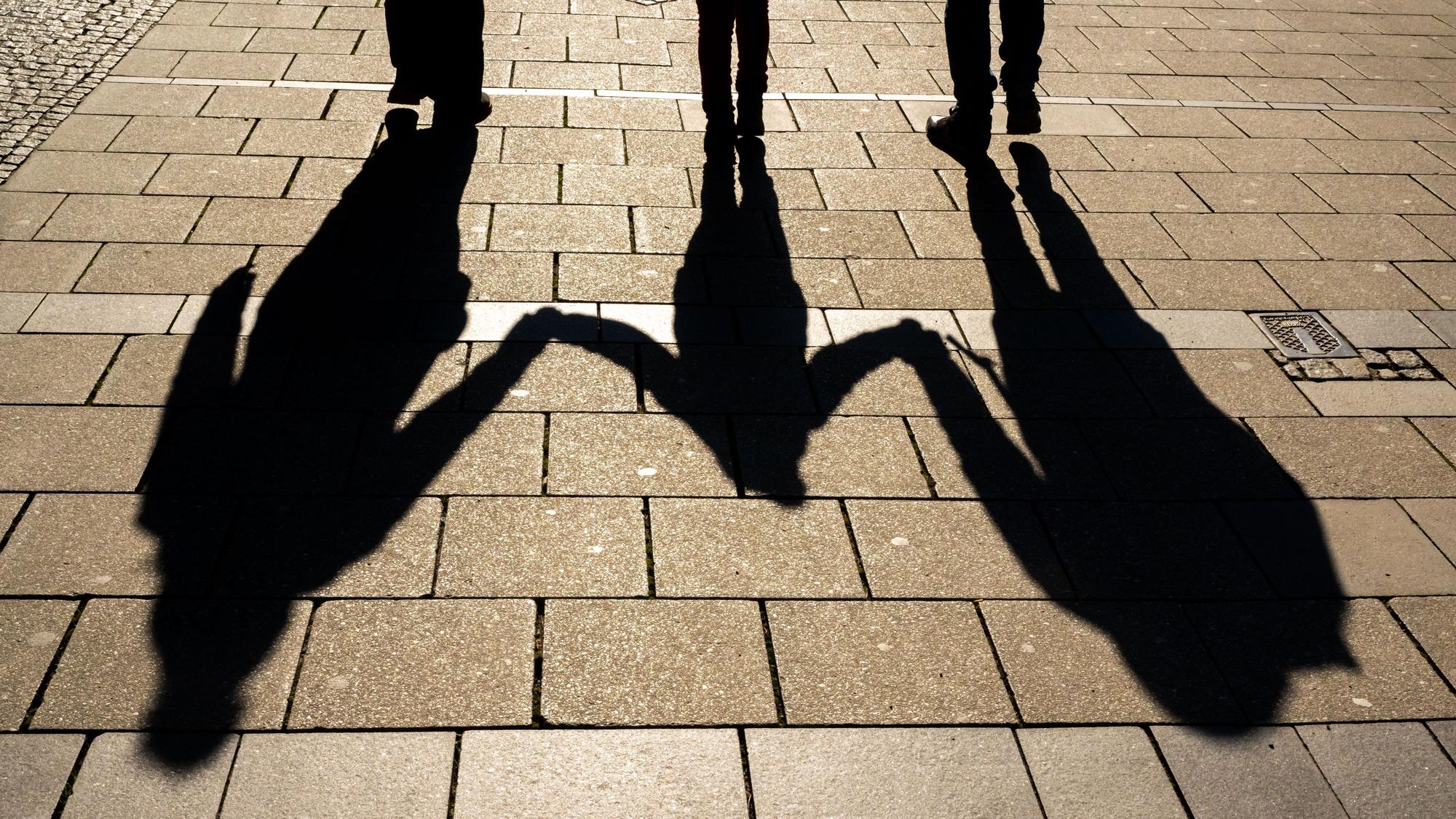 Die Schatten von zwei Erwachsenen und einem Kind sind in den Morgenstunden auf dem Asphalt zu sehen.