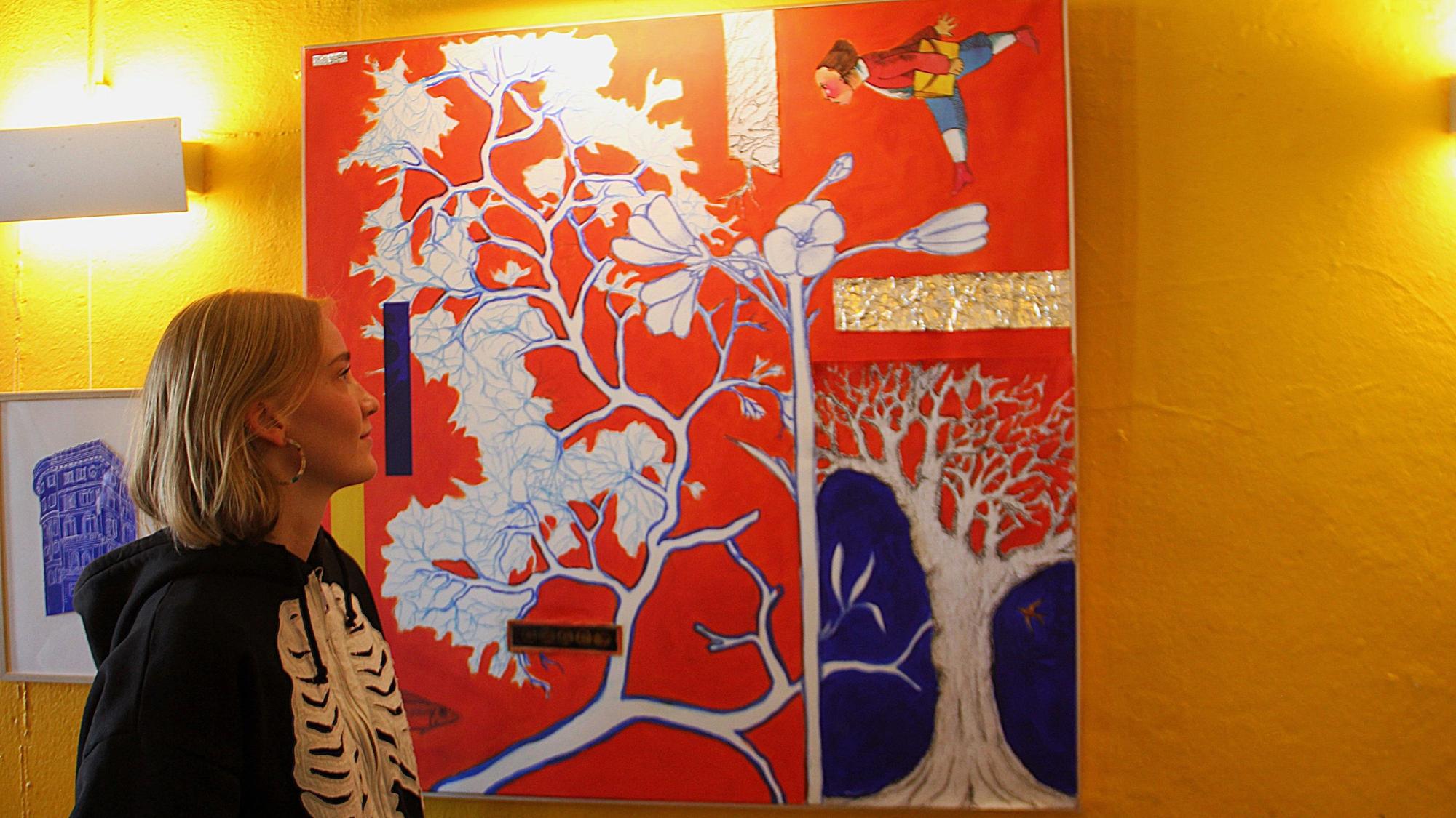 Eine Frau schaut auf ein rot-buntes Bild an einer gelben Wand.